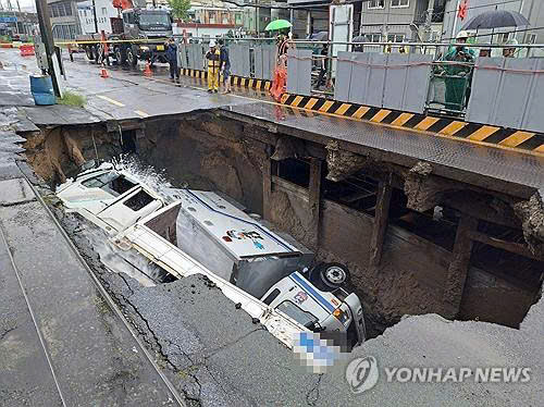 Hai xe tải lọt bên trong hố sụt trên đường phố Busan hôm 21-9. Ảnh Yonhap News